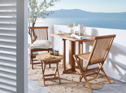 Gartentisch-Set aus Holz auf einem Balkon mit Meerblick, bestehend aus einem Tisch und zwei Stühlen, seitliche Perspektive.