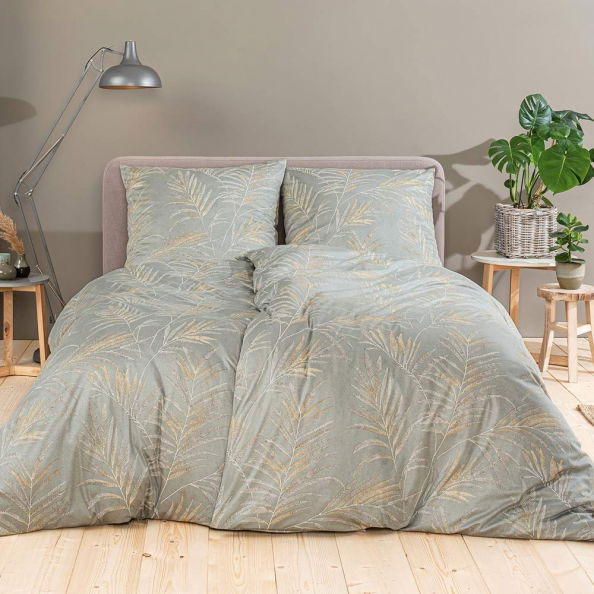 Estella Bettwäsche KENO Bett mit Estella Bettwäsche KENO in sanften Grüntönen und Blattmuster, frontal fotografiert, umgeben von Pflanzen und Holzmöbeln.