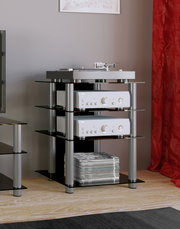 Schwarzes HiFi-Rack mit Glasböden und silbernen Metallstützen, bestückt mit Plattenspieler und zwei silbernen HiFi-Komponenten sowie Magazin-Stapel unten, in seitlicher Perspektive im Wohnzimmer.