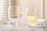 Zwei elegante Trinkgläser POESIA 460ml auf einem Marmortisch, eines gefüllt mit Eis und Zitronenscheiben, aus seitlicher Perspektive fotografiert.