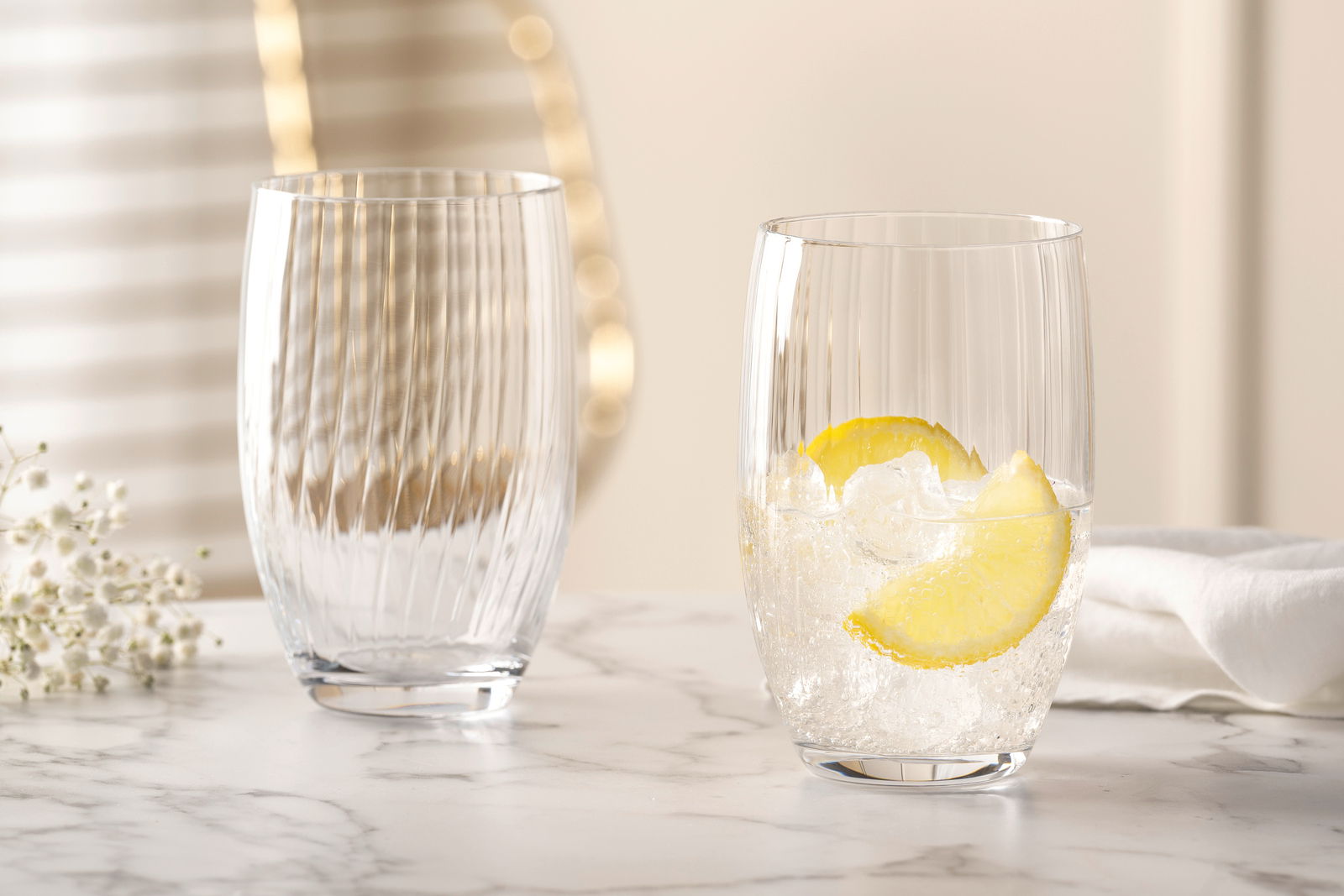 Leonardo Longdrinkbecher POESIA Zwei elegante Trinkgläser POESIA 460ml auf einem Marmortisch, eines gefüllt mit Eis und Zitronenscheiben, aus seitlicher Perspektive fotografiert.