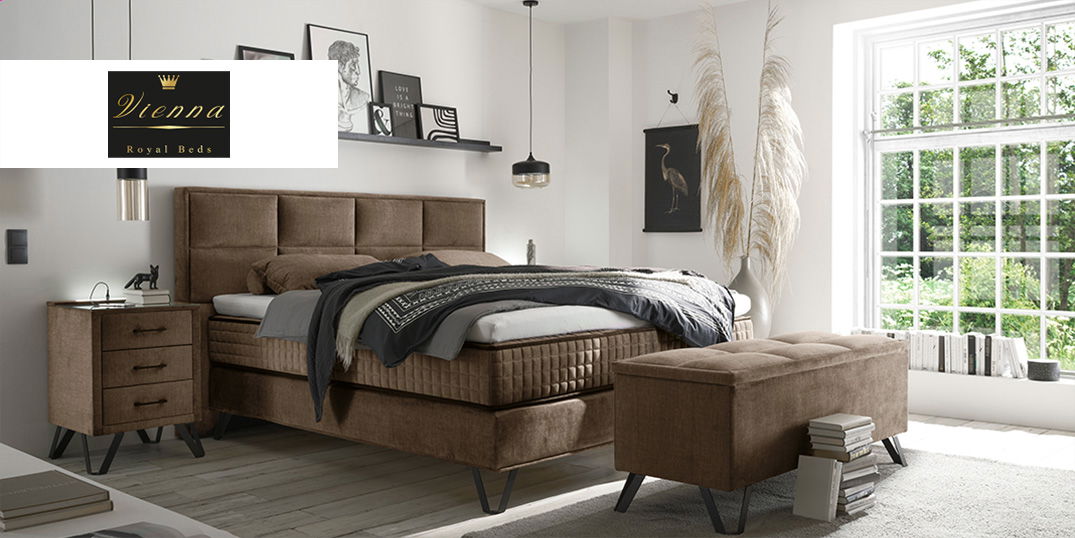 Ein elegantes Schlafzimmer mit braunem Polsterbett, passender Bank und großen Fenstern mit Gartenblick.