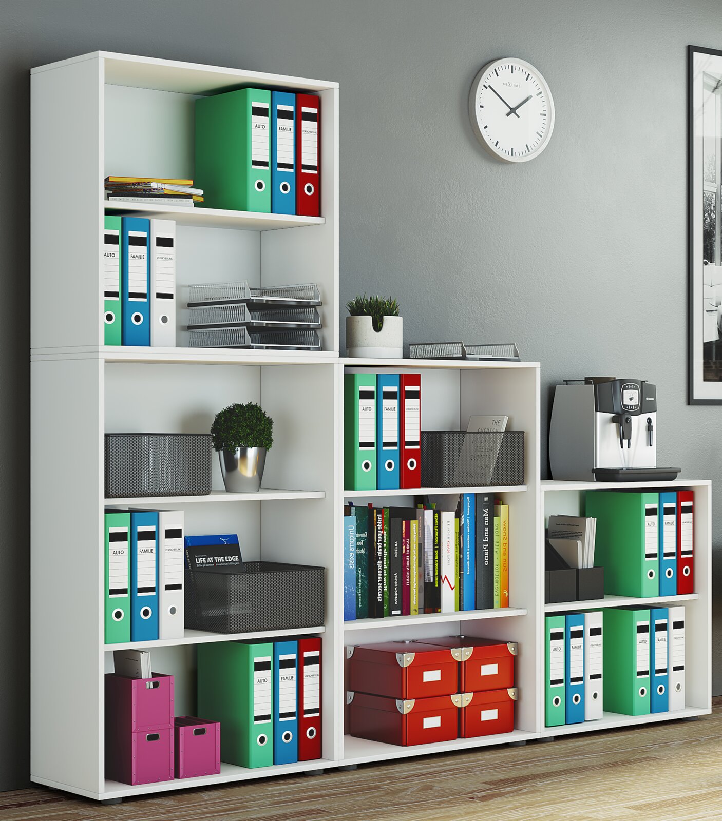 Weißes Büroregal-Set mit offenen Fächern, gefüllt mit bunten Ordnern, Büchern und Aufbewahrungsboxen; seitliche Perspektive im Büro mit Wanduhr und Kaffeemaschine im Hintergrund.