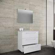 Modernes weißes Badezimmer-Waschtischset mit Unterschrank (drei Schubladen, eine geöffnet), Waschbecken, Armatur und Wandspiegel mit LED-Aufsatzleuchte vor beigefliester Wand, frontale leicht seitliche Perspektive