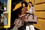Twee vrouwen staan voor een gele container en houden tassen met luipaardprint vast. De tassen zijn van voren te zien.