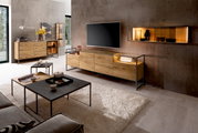 Moderne woonkamer met een Venjakob-dressoir TAGENA van hout en metaal, gezien vanaf de voorkant. Het dressoir staat onder een grote tv, omringd door stijlvolle decoraties en een hangende plank aan de muur.