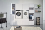 Frontale Ansicht eines modernen Hochschranksystems mit integrierter Waschmaschine und Trockner, umgeben von Stauraum für Wäsche und Reinigungsmittel.
