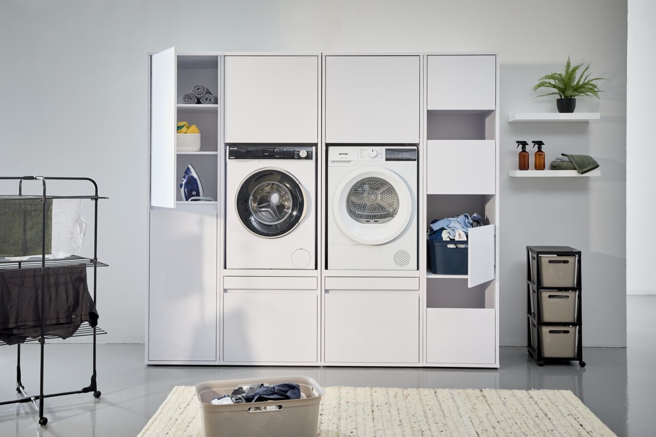 Frontale Ansicht eines modernen Hochschranksystems mit integrierter Waschmaschine und Trockner, umgeben von Stauraum für Wäsche und Reinigungsmittel.