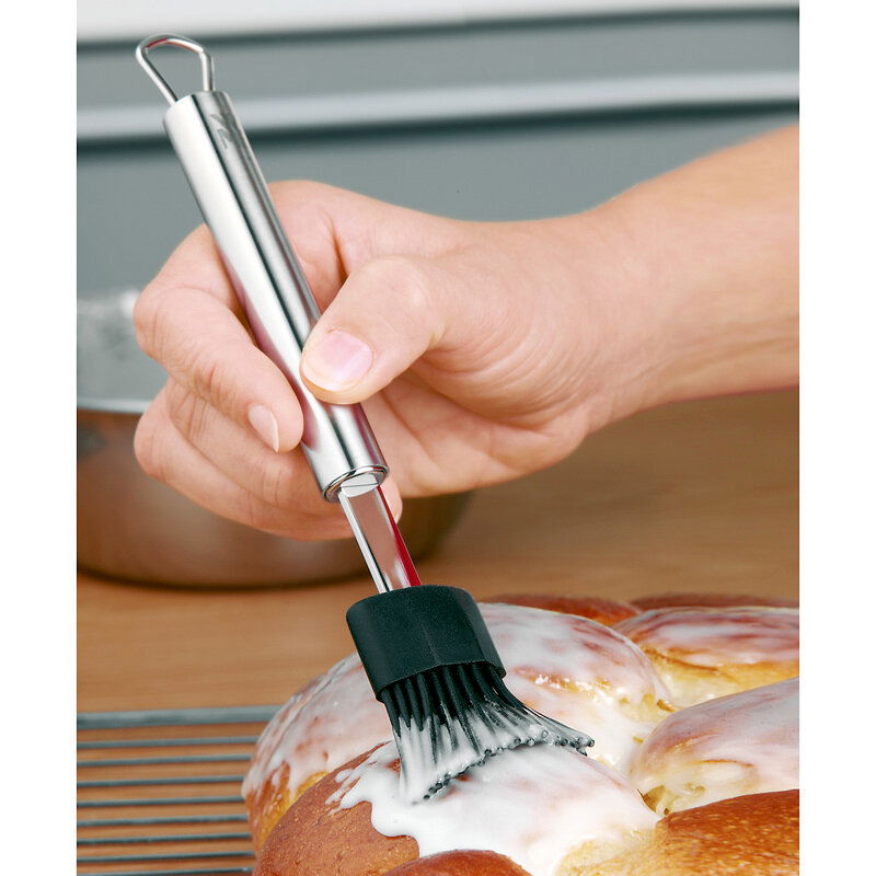 Silikon-Backpinsel PROFI PLUS in der Hand, der Glasur auf einem Gebäck verteilt. Perspektive von der Seite.