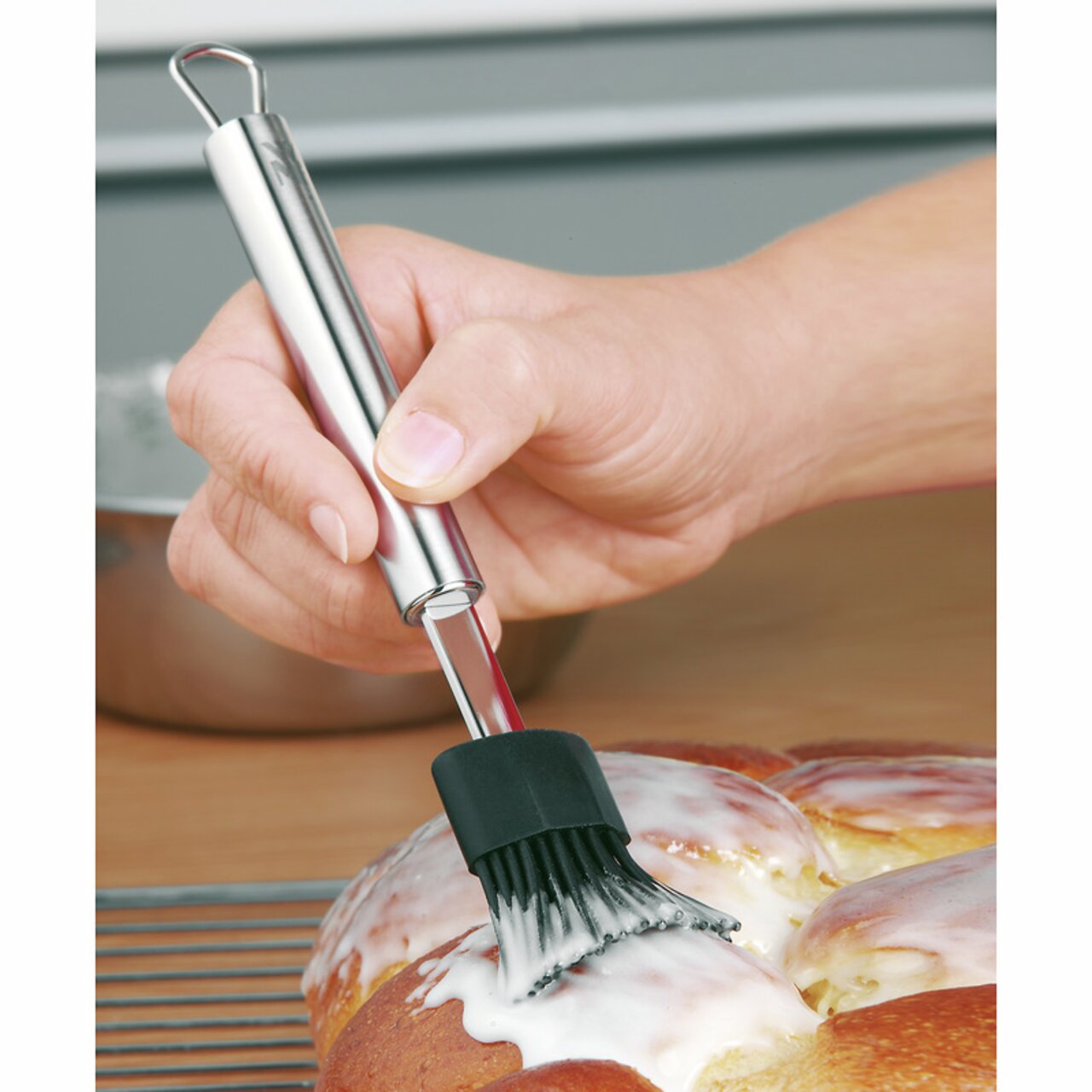 WMF Backpinsel 20cm Silikon-Backpinsel PROFI PLUS in der Hand, der Glasur auf einem Gebäck verteilt. Perspektive von der Seite.