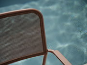 Nahaufnahme eines Stapelsessels mit braunem Metallrahmen und Netzrückenlehne, im Hintergrund ein verschwommener Pool.