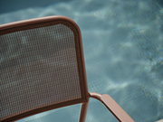 Nahaufnahme eines Stapelsessels mit braunem Metallrahmen und Netzrückenlehne, im Hintergrund ein verschwommener Pool.