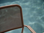 Nahaufnahme eines Stapelsessels mit braunem Metallrahmen und Netzrückenlehne, im Hintergrund ein verschwommener Pool.