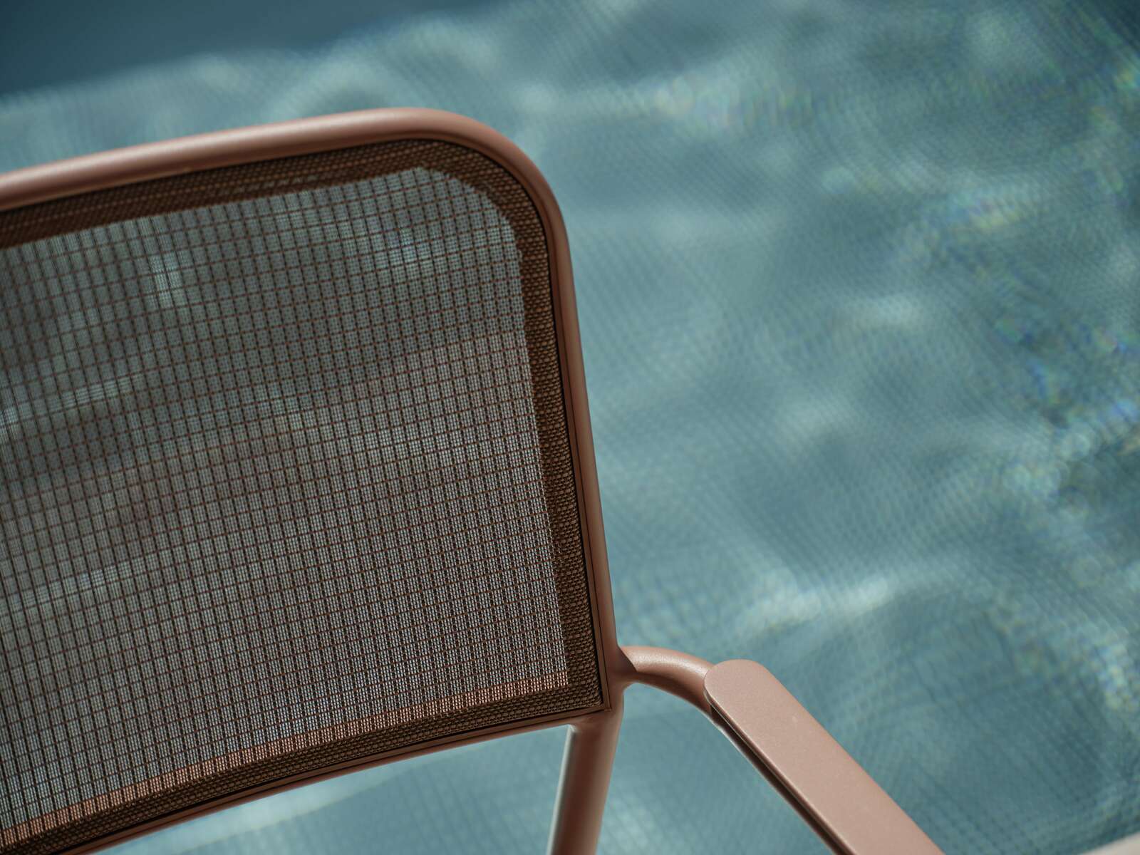 Nahaufnahme eines Stapelsessels mit braunem Metallrahmen und Netzrückenlehne, im Hintergrund ein verschwommener Pool.