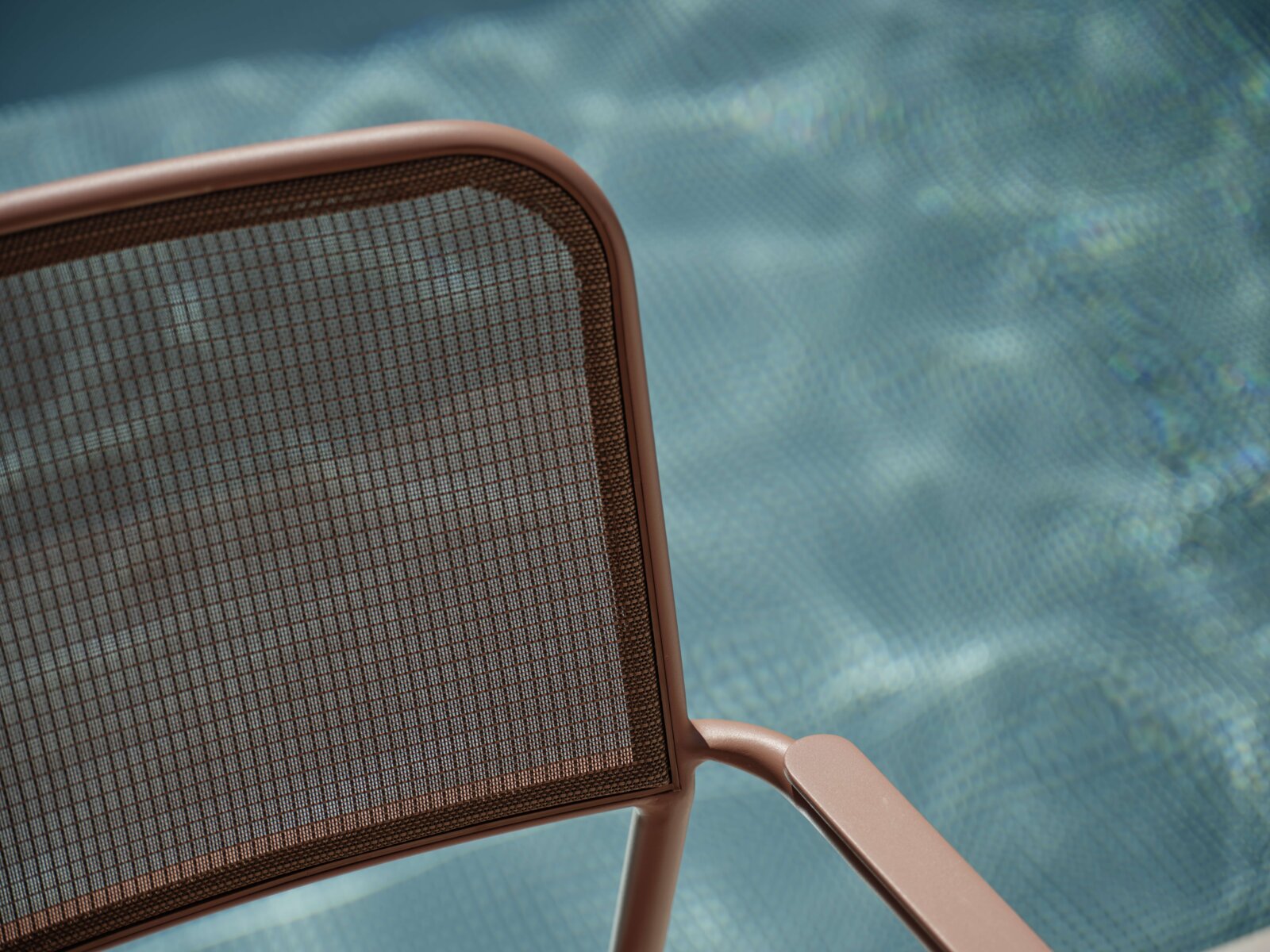 Nahaufnahme eines Stapelsessels mit braunem Metallrahmen und Netzrückenlehne, im Hintergrund ein verschwommener Pool.