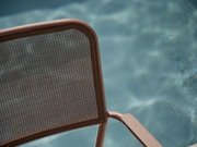 Nahaufnahme eines Stapelsessels mit braunem Metallrahmen und Netzrückenlehne, im Hintergrund ein verschwommener Pool.