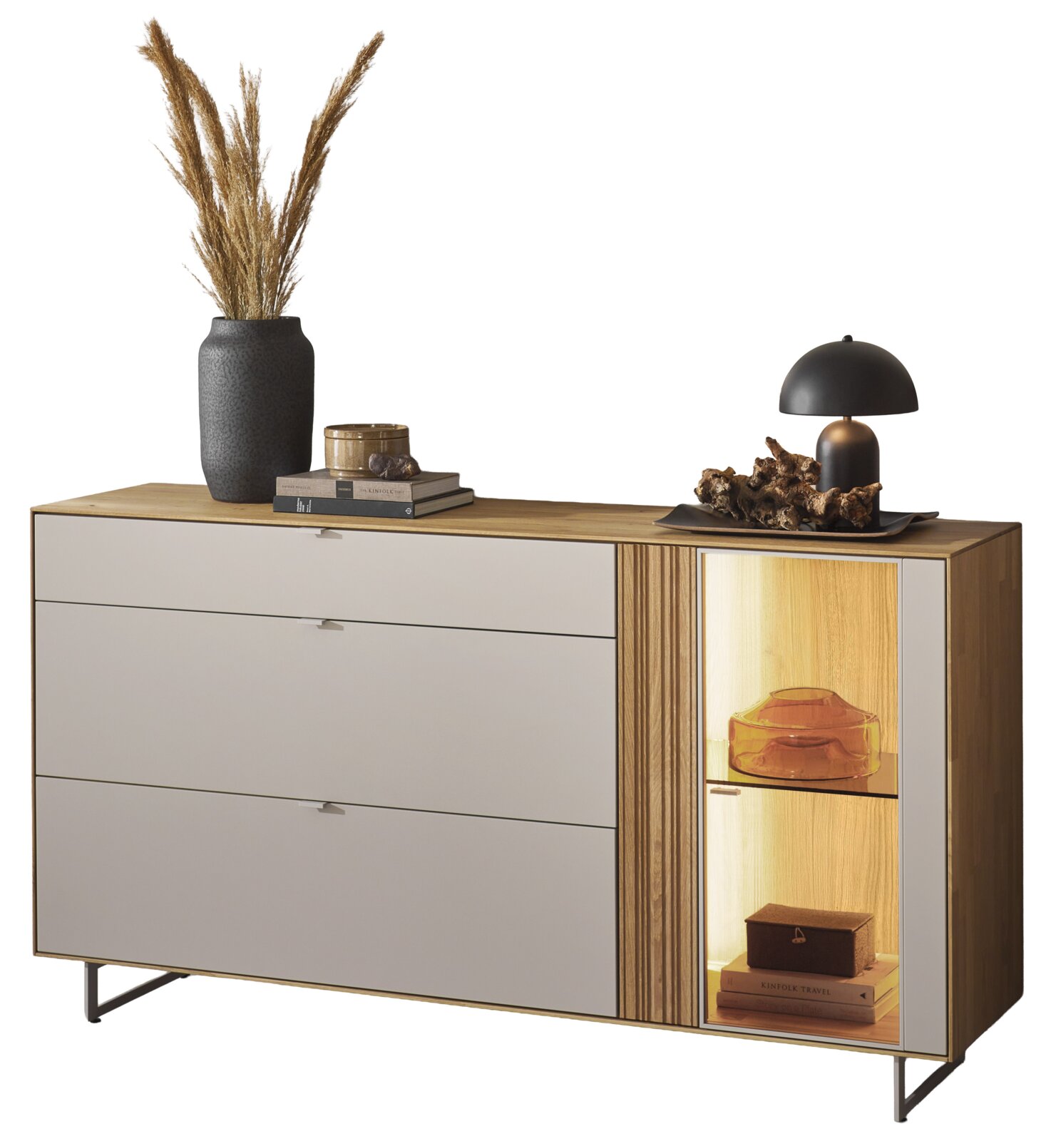 Dieter Knoll Sideboard MALEA Modernes Sideboard aus Holz mit weißer Front und beleuchtetem Vitrinenfach, dekoriert mit Vase, Büchern und Tischlampe, in Frontansicht leicht von rechts.