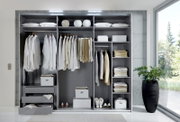 Offener Schwebetürenschrank mit drei Türen, gefüllt mit Kleidung, Kissen und Accessoires, von vorne betrachtet.