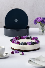 Runde Backform mit abnehmbarem Boden, präsentiert mit einer dekorierten Torte, umgeben von Blumen und Beeren, aus der Vogelperspektive.