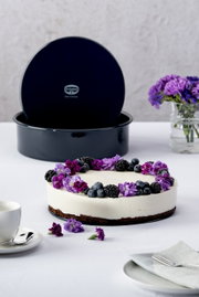 Runde Backform mit abnehmbarem Boden, präsentiert mit einer dekorierten Torte, umgeben von Blumen und Beeren, aus der Vogelperspektive.