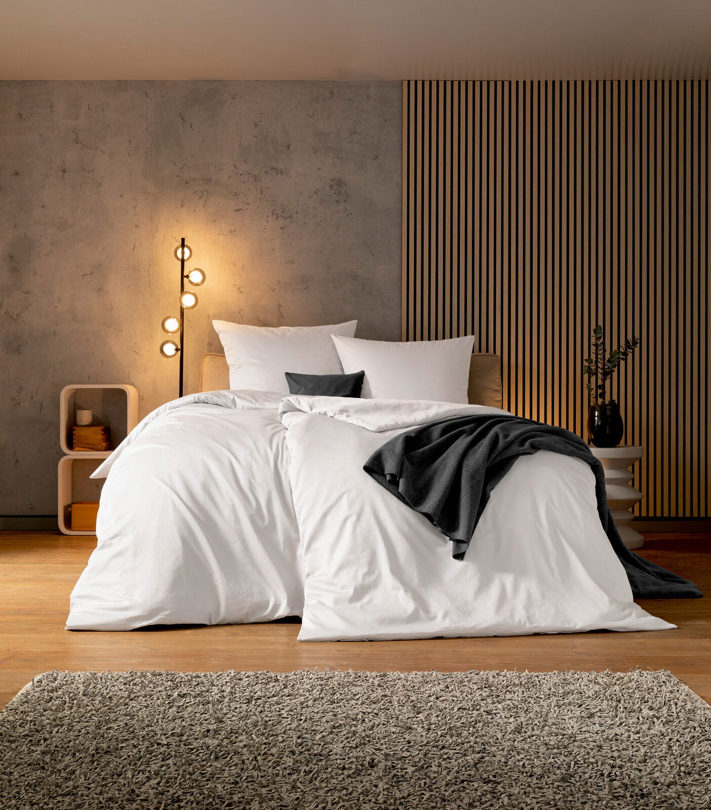 Gemütliches Schlafzimmer mit moderner Bettwäsche in Weiß, frontal fotografiert, mit dekorativen Kissen und einer stilvollen Stehlampe im Hintergrund.