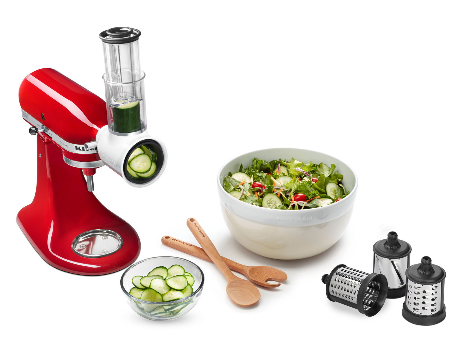 Roter Gemüseschneider mit Schnitzwerk, von der Seite gezeigt, neben einer Schüssel mit frischem Salat und verschiedenen Schneideaufsätzen.
