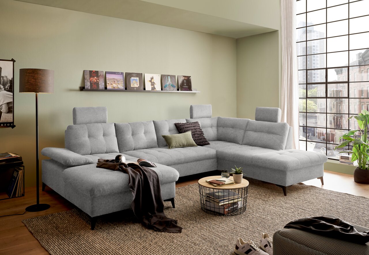 Z2 Wohnlandschaft DURBAN Graues Ecksofa in einem modernen Wohnzimmer, mit Blick von vorne. Das Sofa hat verstellbare Kopfstützen und ist mit Kissen dekoriert. Ein Couchtisch und Dekorationen ergänzen das gemütliche Ambiente.