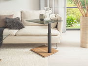 Moderner Beistelltisch mit Glasplatte und Holzfuß, seitliche Perspektive neben einem Sofa.