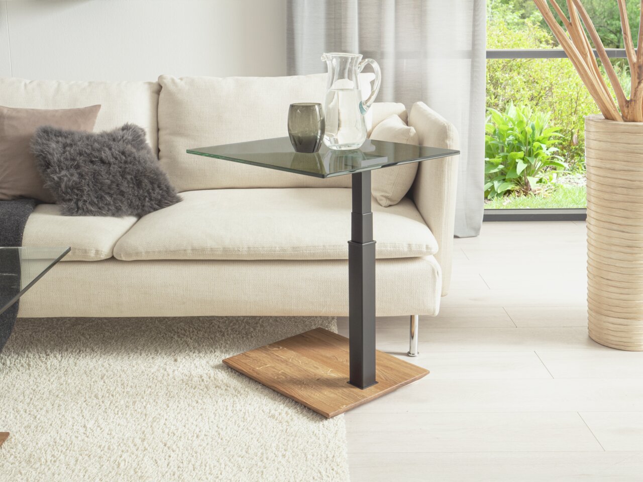 Moderner Beistelltisch mit Glasplatte und Holzfuß, seitliche Perspektive neben einem Sofa.