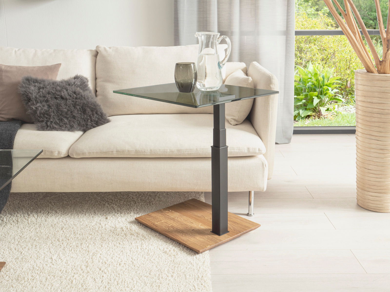 Moderner Beistelltisch mit Glasplatte und Holzfuß, seitliche Perspektive neben einem Sofa.