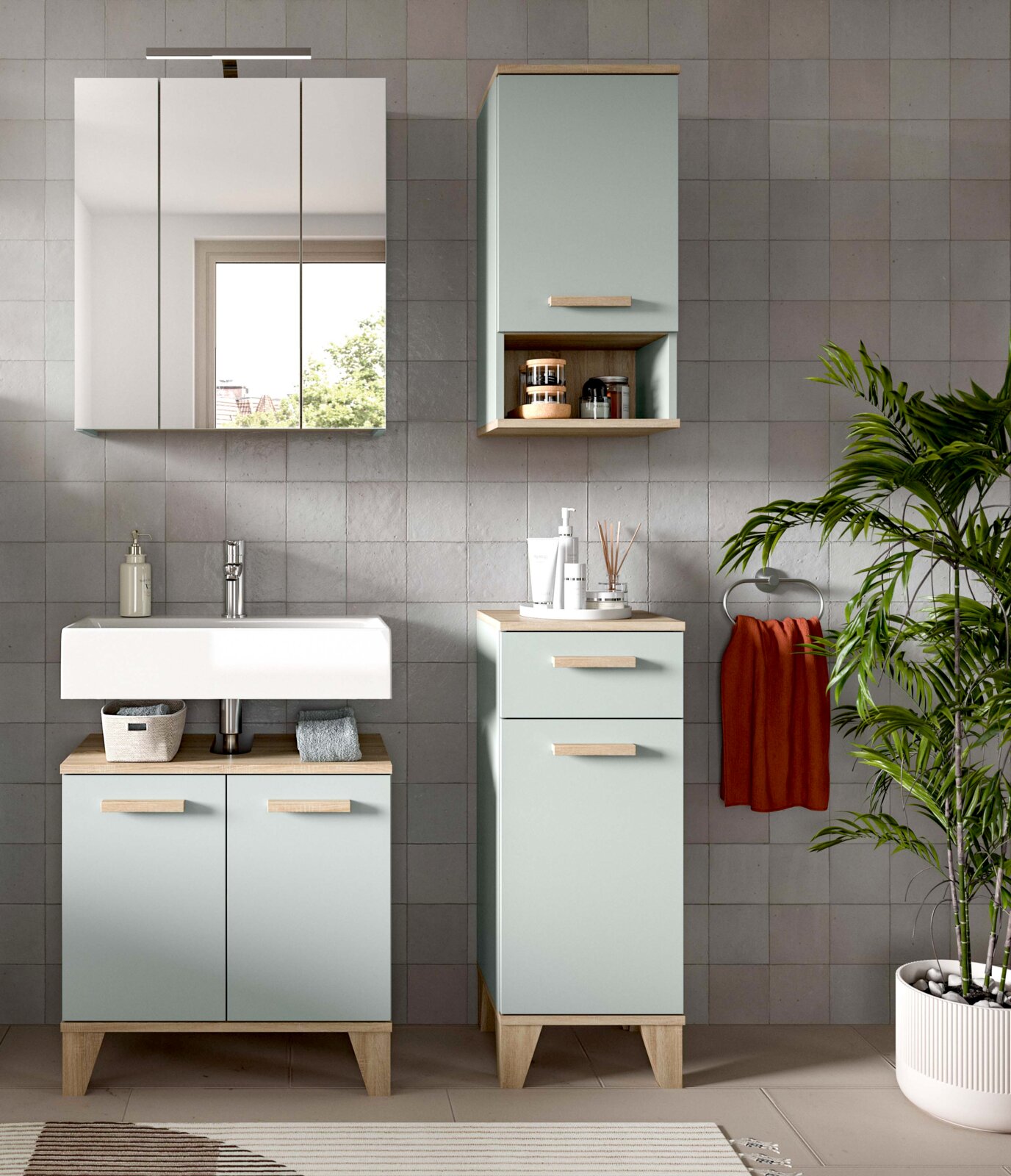 Modernes Badmöbel-Set in Mintgrün mit Holzgriffen und Holzplatte, Waschbecken-Unterschrank, Spiegelschrank sowie Hochschrank mit offenem Regal an grauer Fliesenwand, Frontalansicht auf Augenhöhe.