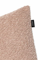 Nahaufnahme einer beigen Zierkissenhülle mit strukturierter Oberfläche und einem kleinen schwarzen Etikett an der Seite. Perspektive von der Ecke des Kissens.