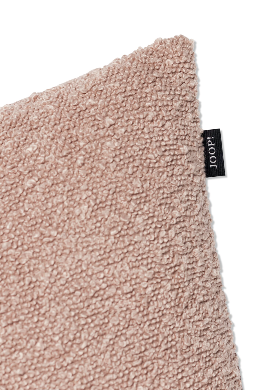 Nahaufnahme einer beigen Zierkissenhülle mit strukturierter Oberfläche und einem kleinen schwarzen Etikett an der Seite. Perspektive von der Ecke des Kissens.