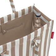 Schuin aanzicht van bovenaf van een beige-wit gestreepte boodschappentas met binnenvak en flessenhouder, met daarin een klein glazen flesje; aan de zijkant is het rode reisenthel-label zichtbaar.