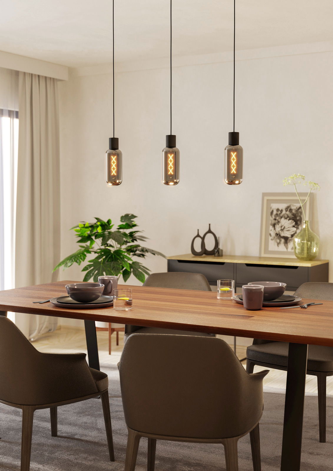 Drei moderne Pendelleuchten MAIONE hängen über einem Esstisch in einem stilvoll eingerichteten Raum, seitliche Perspektive.