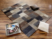 Moderner Wollteppich mit geometrischem Muster in Erdtönen, auf einem Holzboden liegend, mit zwei Kissen und einem Tablett mit Zeitschriften. Perspektive von oben.