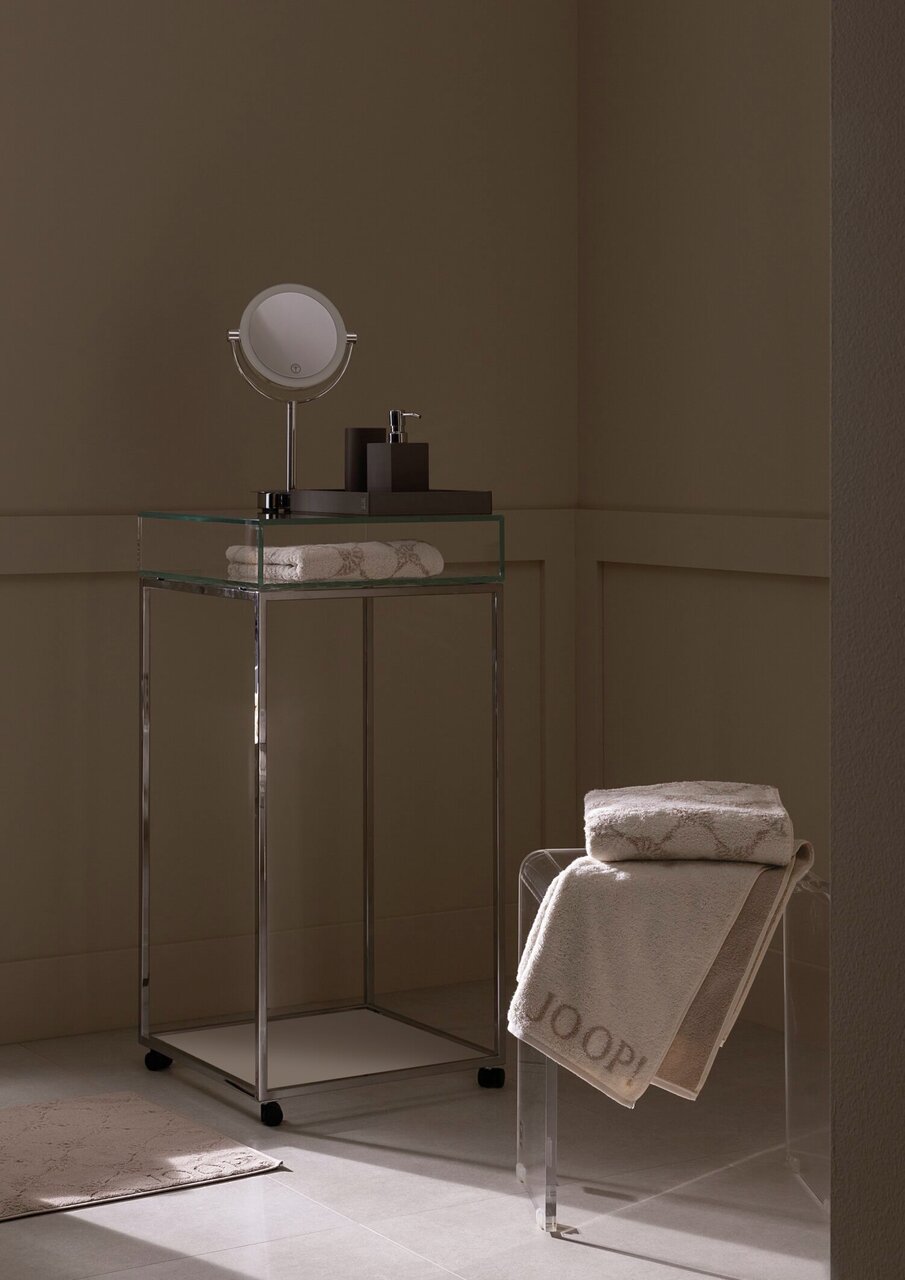 Een luxe douchehanddoek in een stijlvolle badkamer, gedrapeerd over een doorzichtige stoel, met een elegant ontwerp en het opschrift 'JOOP!' in zijaanzicht.