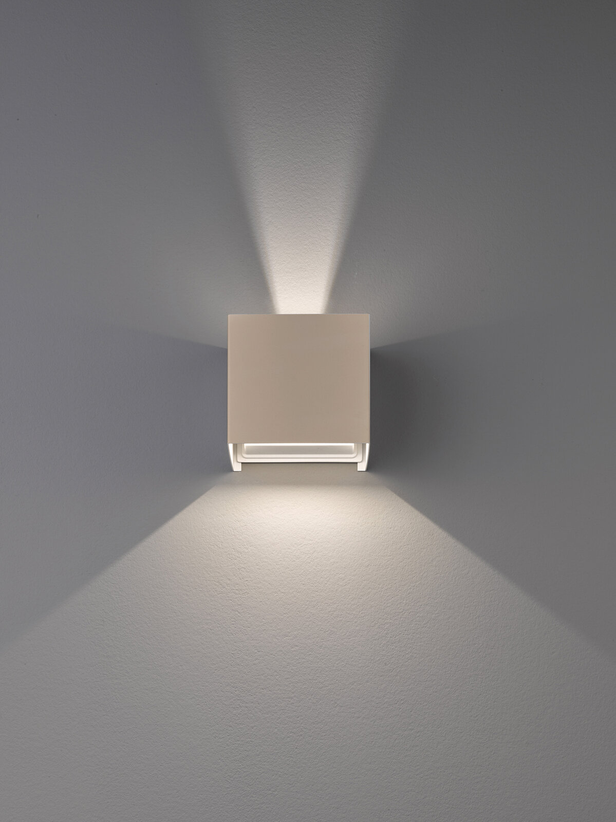 Moderne, quadratische Wandleuchte in Weiß mit Up-&-Down-Light, frontal von vorn an der Wand fotografiert, wirft symmetrische Lichtkegel nach oben und unten.