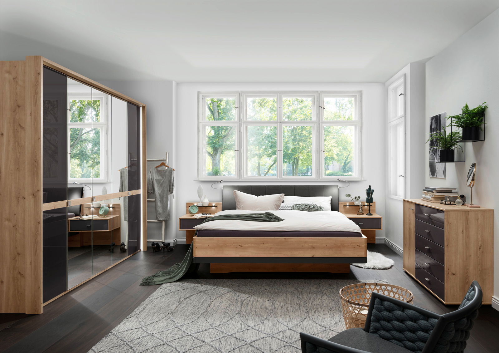 Modernes Schlafzimmer mit Futonbett aus Holz, umgeben von stilvollen Möbeln und großen Fenstern, die einen Blick ins Grüne bieten. Perspektive von vorne auf das Bett.