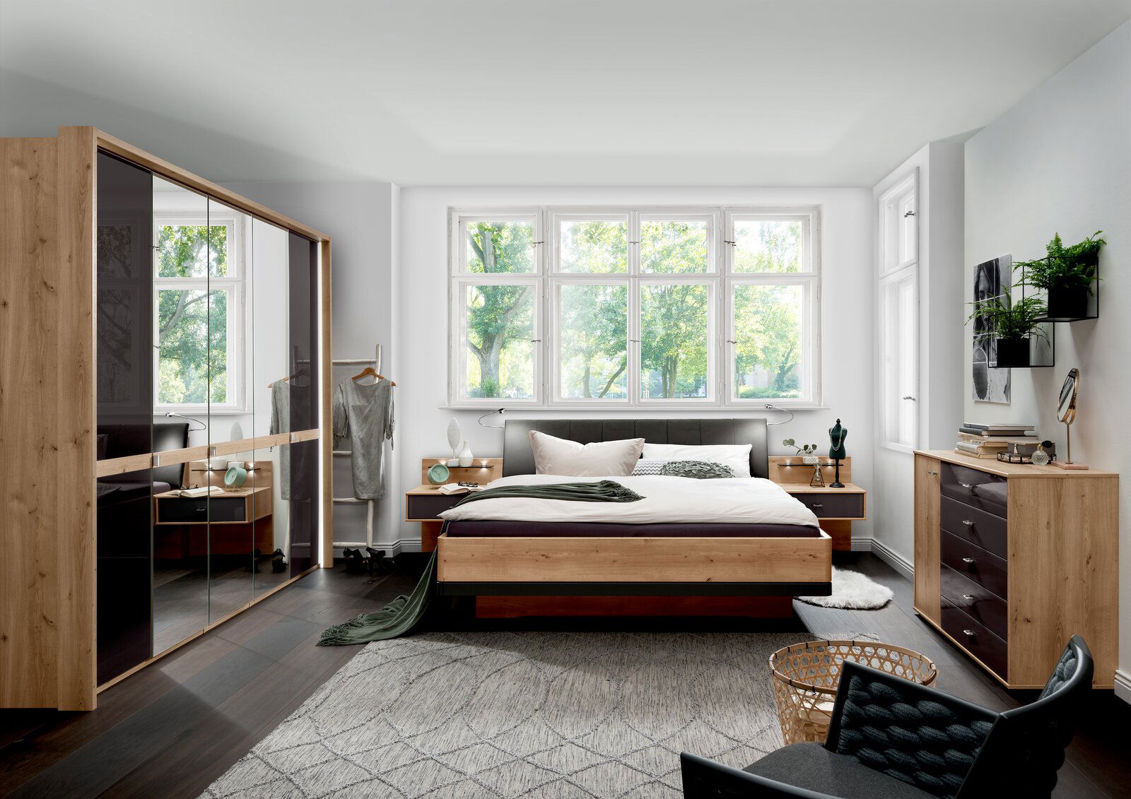 Modernes Schlafzimmer mit Futonbett aus Holz, umgeben von stilvollen Möbeln und großen Fenstern, die einen Blick ins Grüne bieten. Perspektive von vorne auf das Bett.