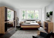 Moderne slaapkamer met een houten futonbed, omringd door stijlvolle meubels en grote ramen die uitzicht bieden op de groene omgeving. Aanzicht van voren op het bed.
