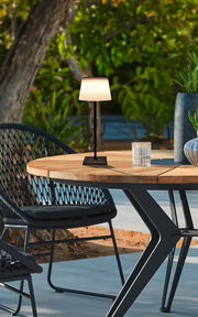 Solarleuchte auf einem Holztisch im Freien, umgeben von Gartenmöbeln und Pflanzen, seitliche Perspektive