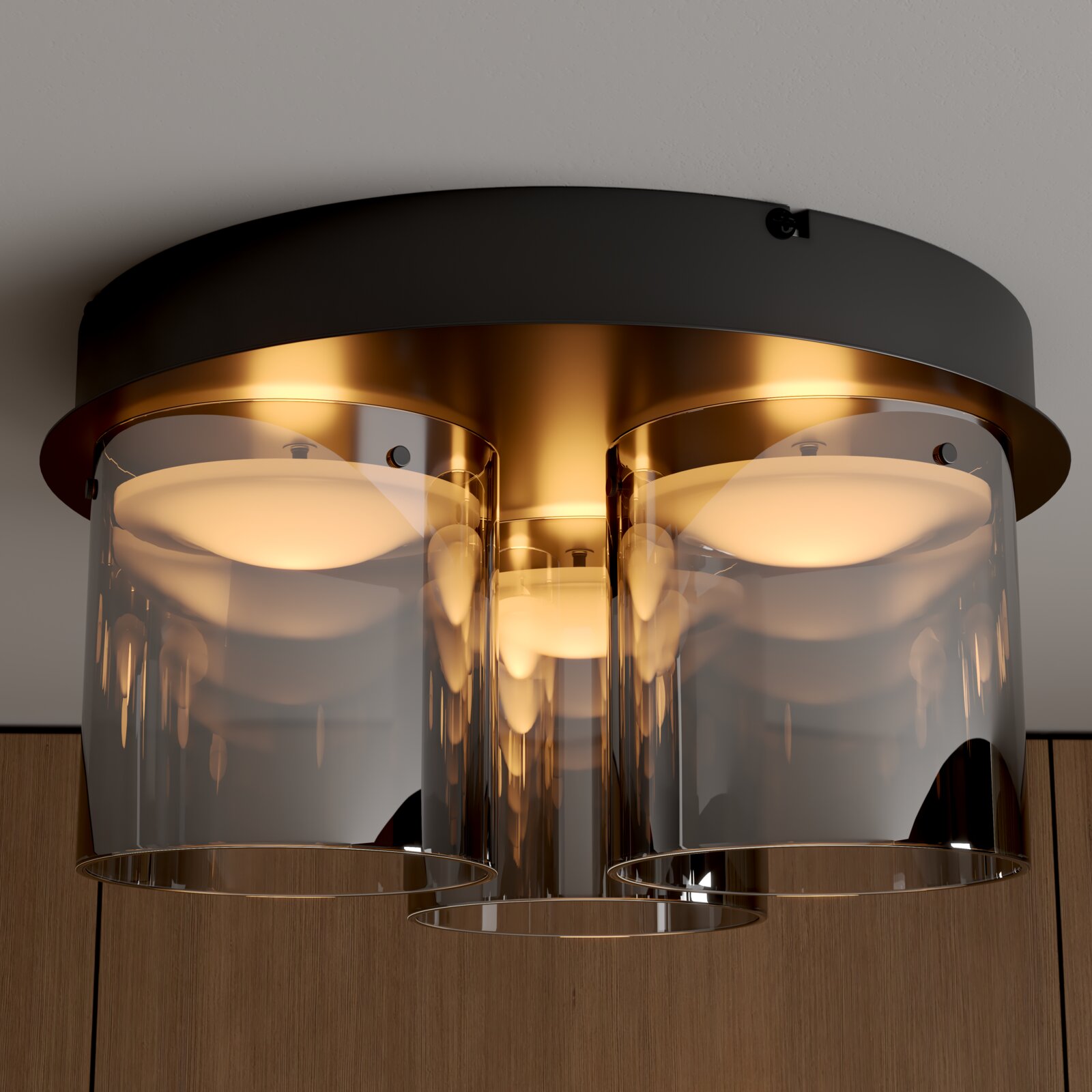 Moderne Deckenleuchte mit schwarzem Baldachin, goldfarbenem Innenkörper und drei rauchgrauen Glaszylindern, leuchtend in warmer Lichtfarbe, Nahaufnahme von unten (Untersicht)