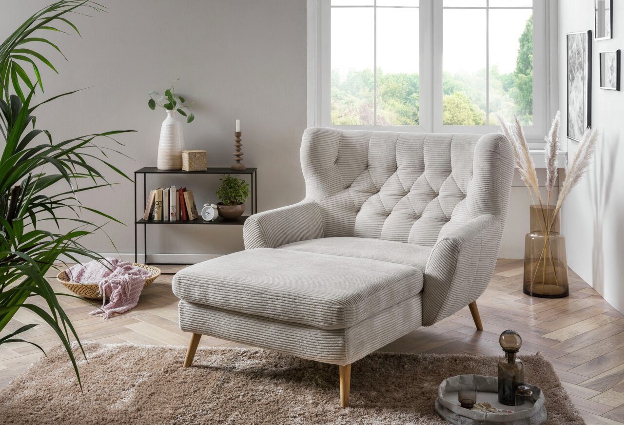Gemütlicher Big Sessel in einem modernen Wohnzimmer, seitliche Perspektive, mit hellgrauem Stoff und Holzbeinen, umgeben von Pflanzen und Dekorationen.