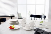 Elegantes weißes Kaffeeservice mit Tassen und Untertassen auf einem Tisch, seitliche Perspektive.