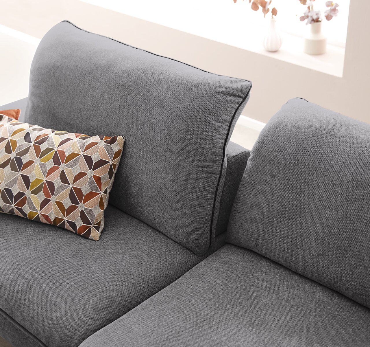 Grijze longchair-bank met kussens met geometrisch patroon, gezien vanaf de zijkant.
