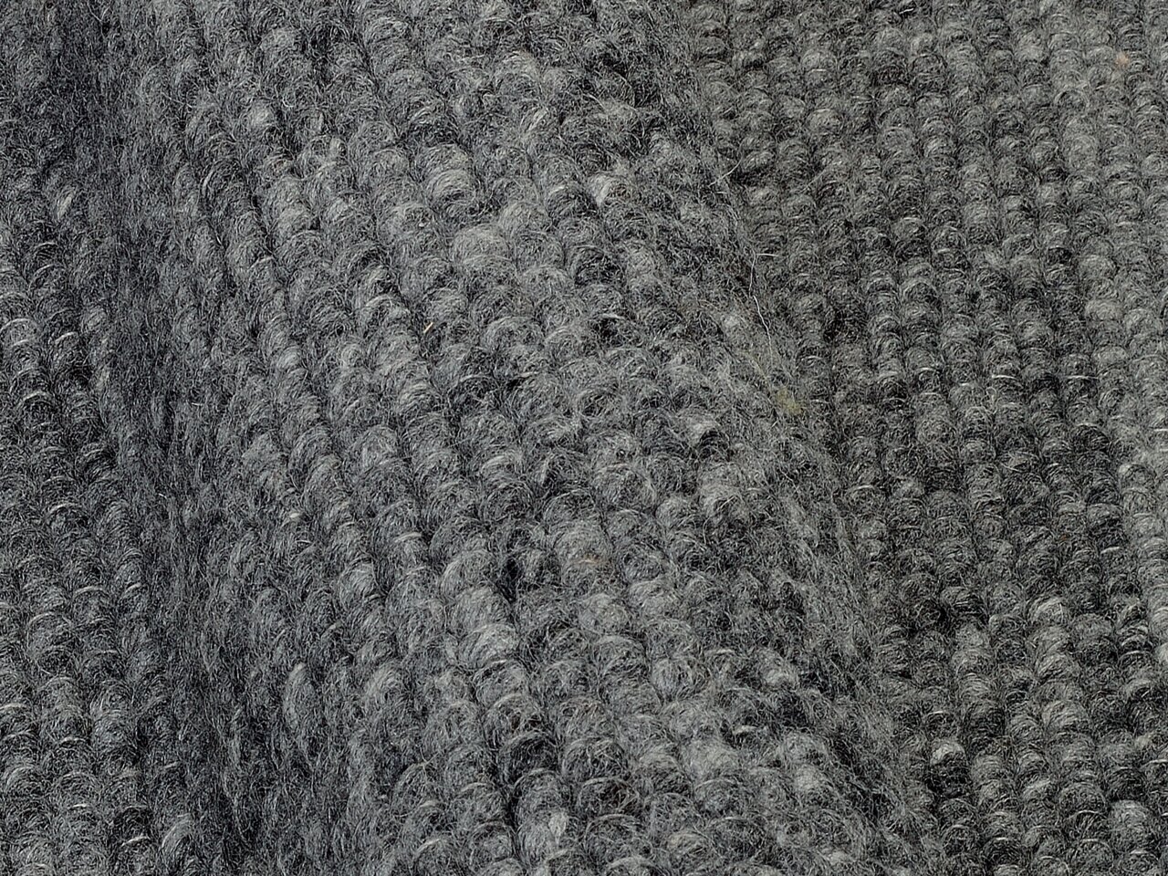 Nahaufnahme eines grauen Handweb Teppichs mit strukturierter Oberfläche in diagonaler Perspektive.