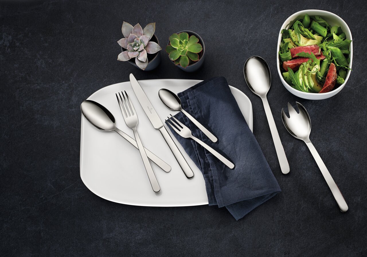 Villeroy & Boch Besteck Louis 68-tlg. LOUIS Vogelperspektive auf ein elegantes 68-teiliges Besteckset 'Louis' auf einem weißen Teller mit blauer Serviette, umgeben von Salat und Sukkulenten.