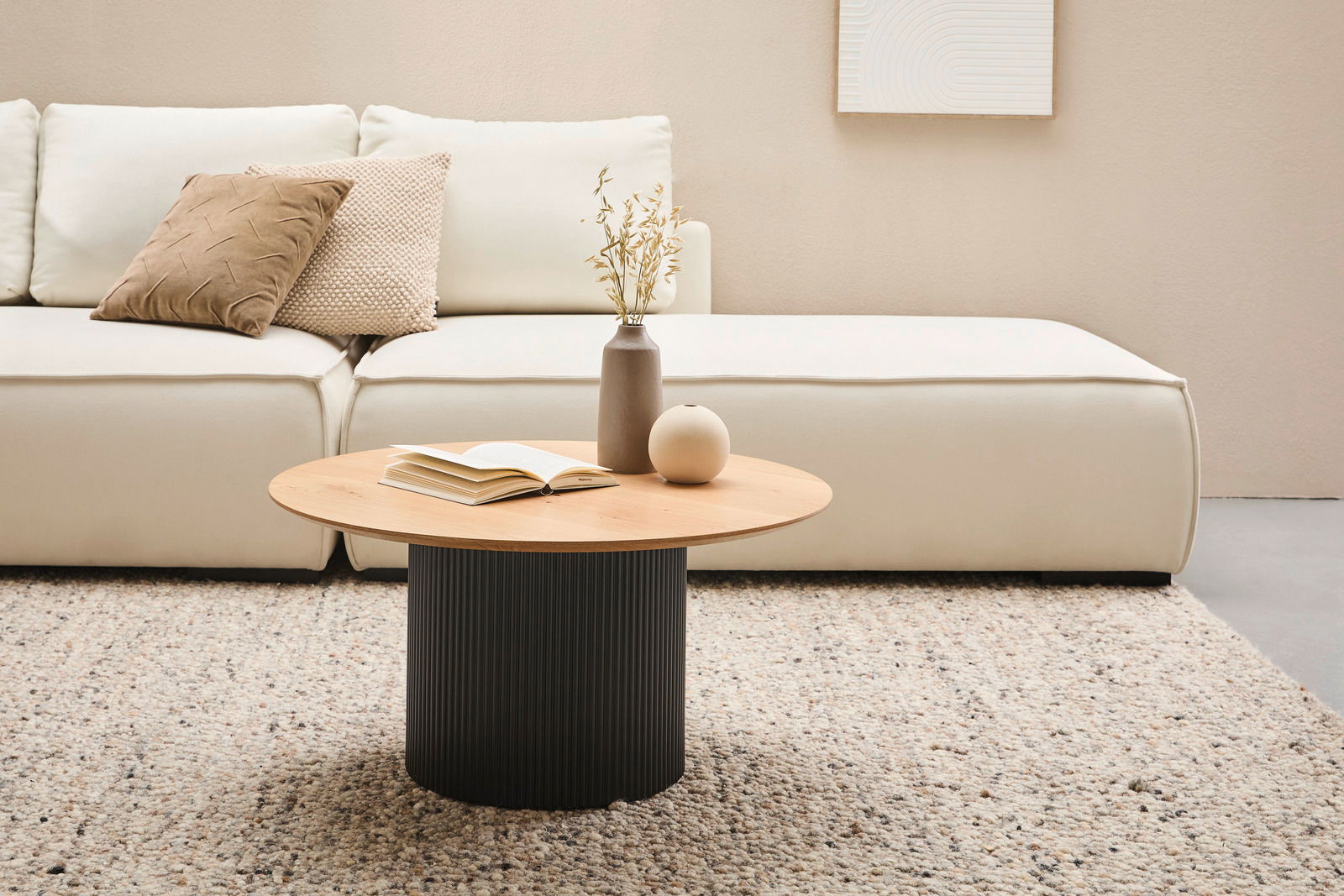 Stylife Couchtisch GROOVE WOOD Moderner Couchtisch mit runder Holzplatte und geriffeltem schwarzen Sockel, im Wohnzimmer vor einem cremefarbenen Sofa, aus der Frontalperspektive.