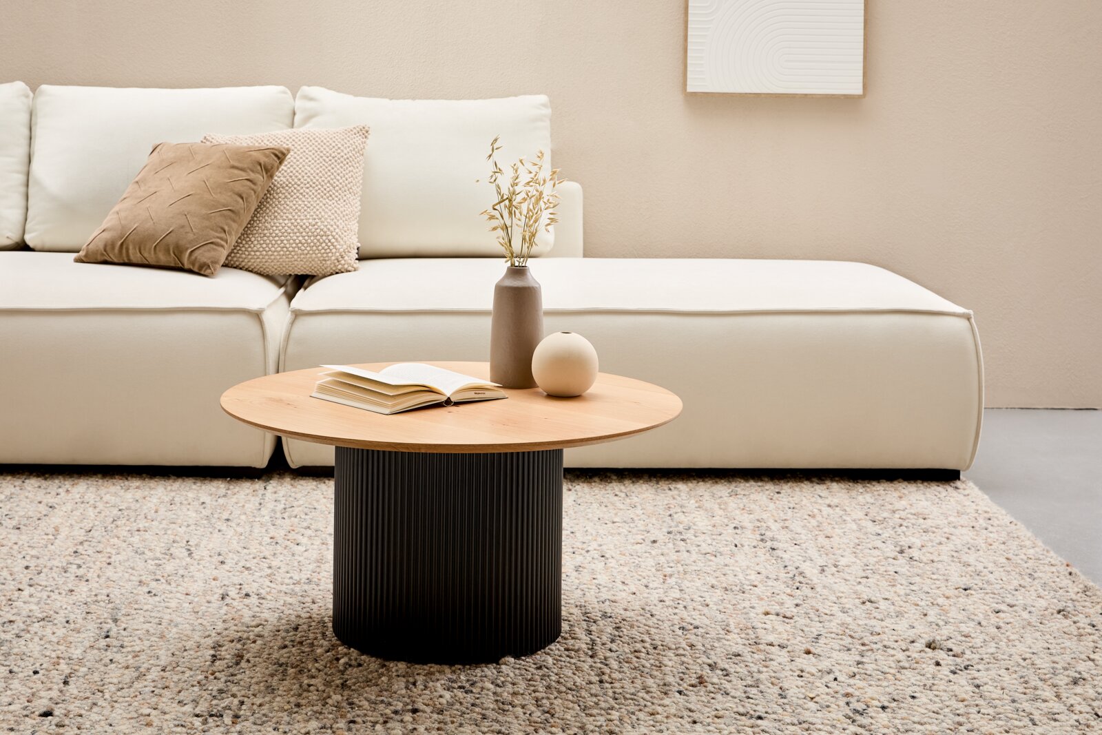 Stylife Salontafel GROOVE WOOD Moderne salontafel met een rond houten blad en een geribbelde zwarte voet, in de woonkamer voor een crèmekleurige bank, gezien van voren.